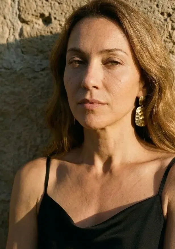 Porträt einer Frau mit goldenem Ohrring vor einer sonnenbeschienenen Steinwand