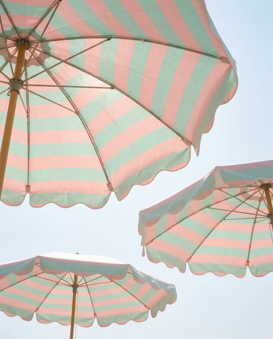 Drei rosa-mintfarben gestreifte Sonnenschirme vor hellem Himmel